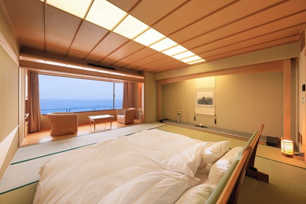 A room with a bed, a small table, a chair, a view of the sea, and a wall-mounted shelf with a vase. - Wakamatsu Hot Spring Resort (Hakodate)