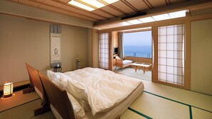 Una habitación tradicional japonesa con suelo de tatami, una cama, un televisor y vistas al mar.