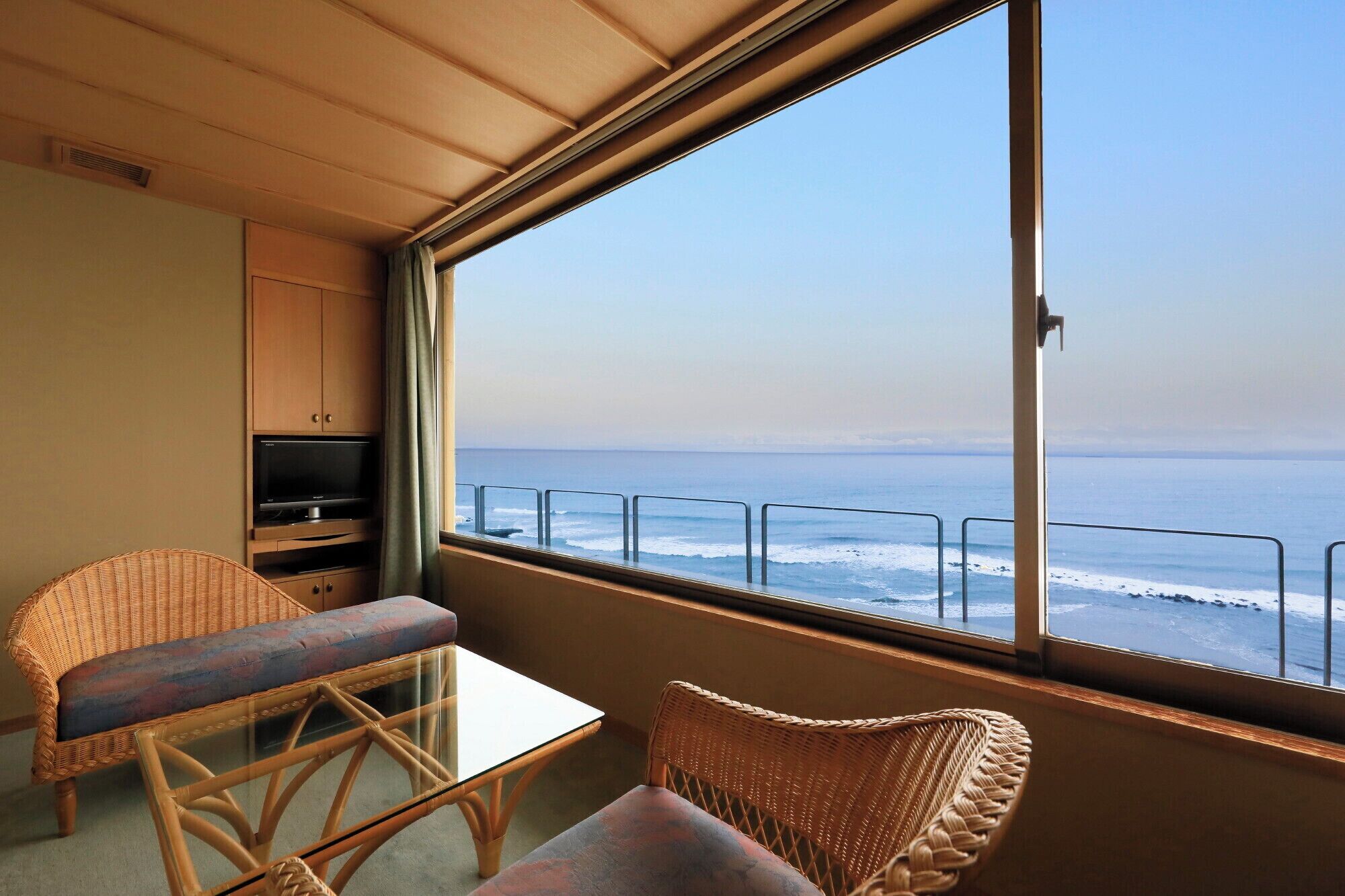 A balcony with wicker furniture, a glass table, and a view of the ocean.