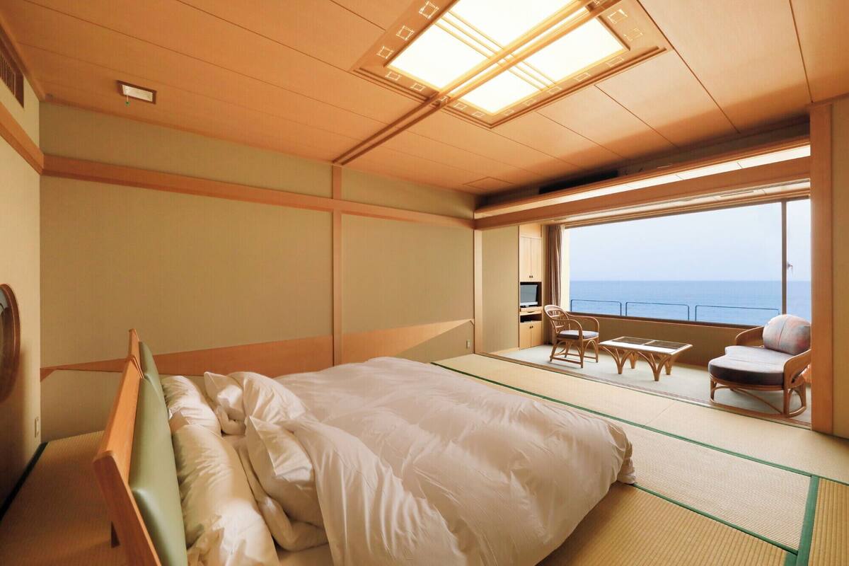 A room with a bed, a small table, chairs, and a view of the sea.
