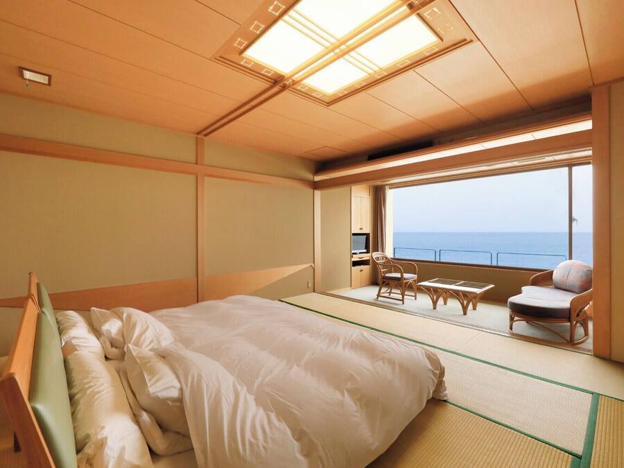 A room with a bed, a small table, chairs, and a view of the sea.