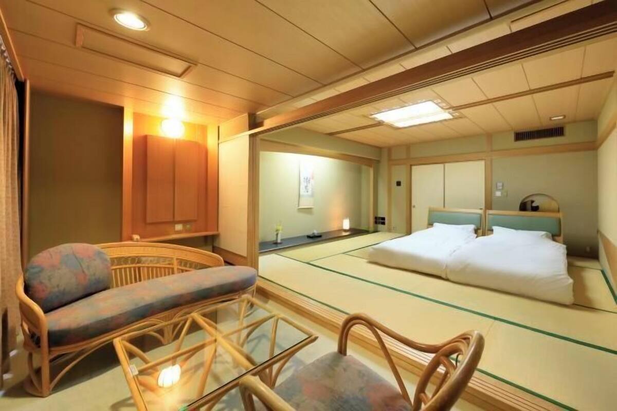 A traditional Japanese room with tatami flooring, a low wooden bed, a cushioned bench, and a glass table.