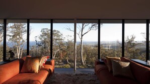A modern living room with a large window offering a scenic view of trees and hills.
