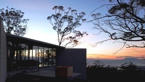 A modern building with large windows, a patio area, and a view of the sunset over the ocean.