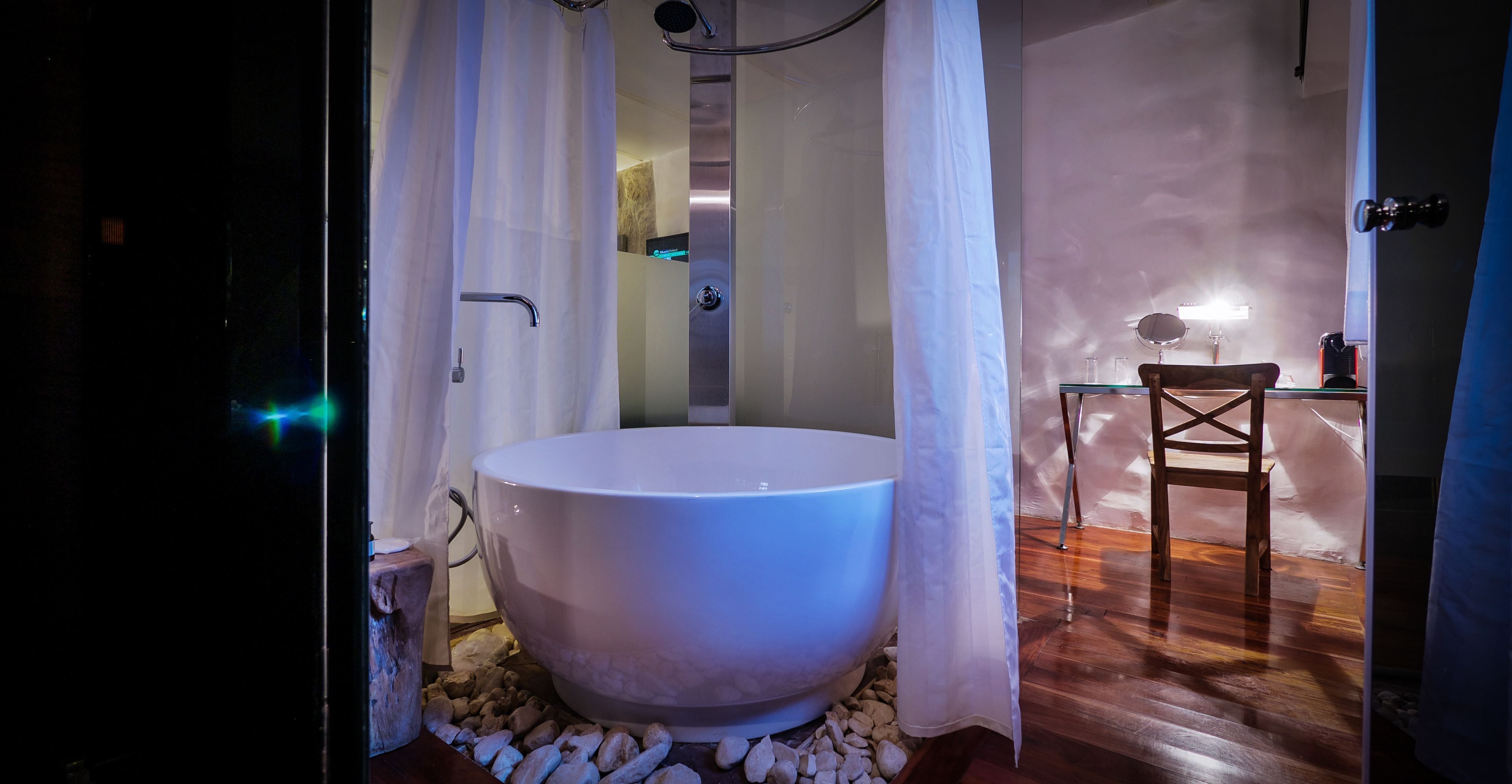 A large, white freestanding bathtub in a modern bathroom with a wooden floor and a glass table.