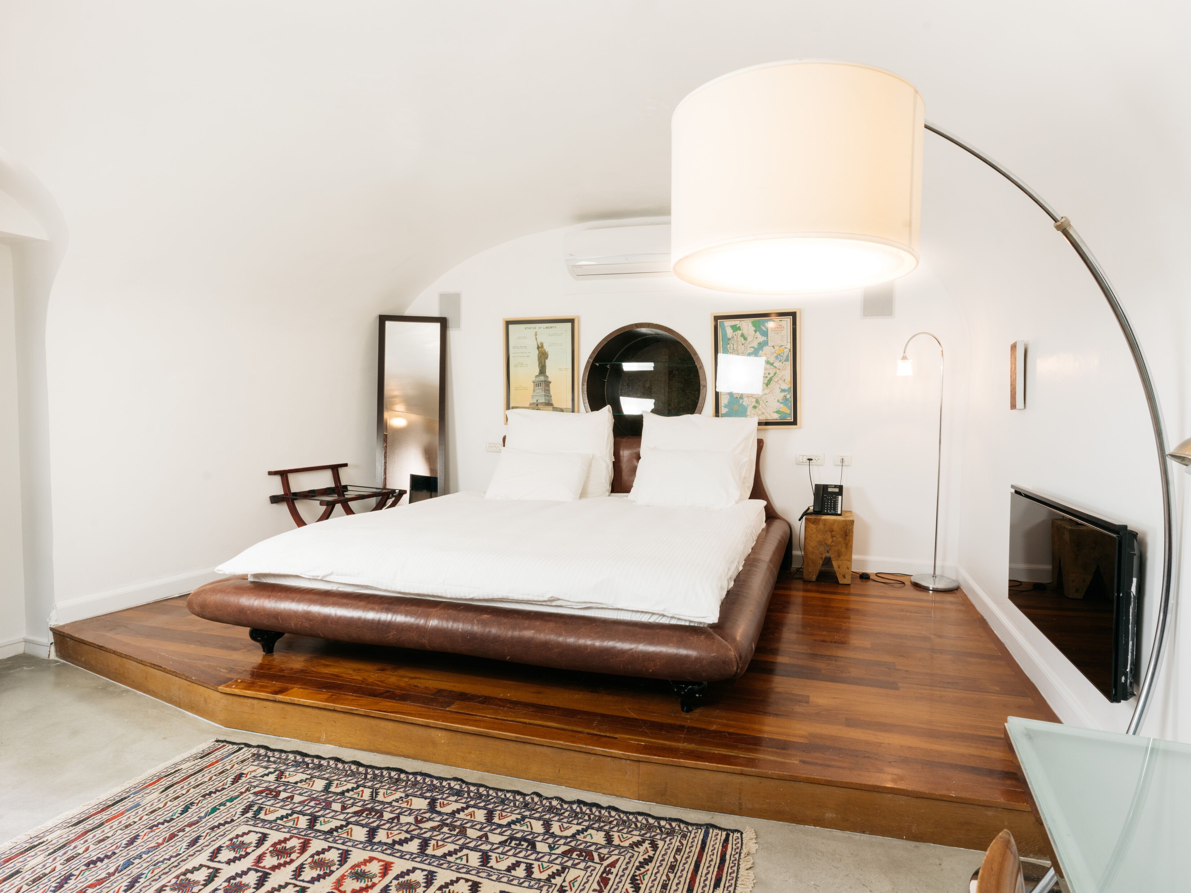 Un dormitorio moderno con una cama grande, una plataforma de madera, una alfombra estampada y un espejo grande.
