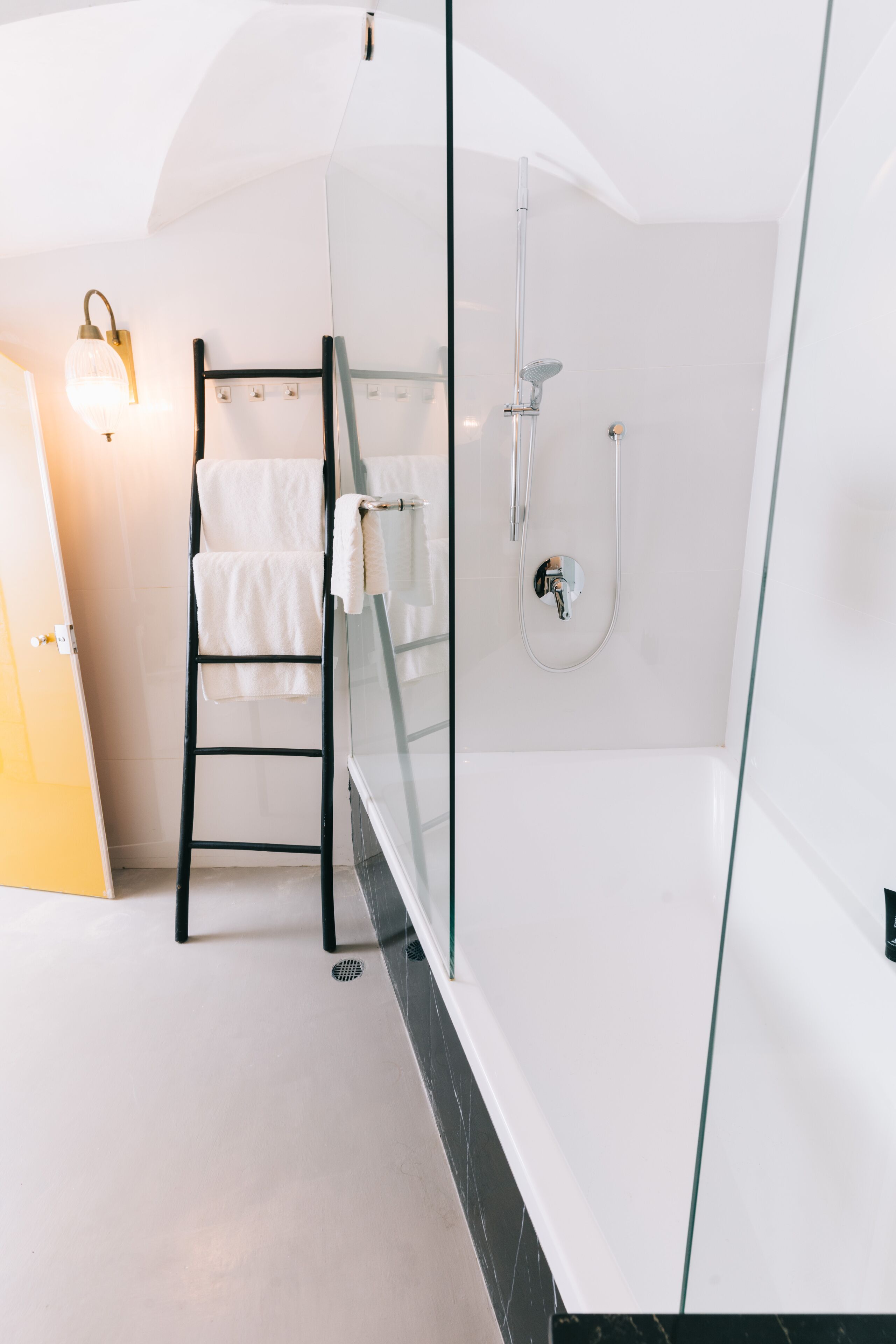 A modern bathroom with a glass shower enclosure, a black metal ladder, and a white bathtub.