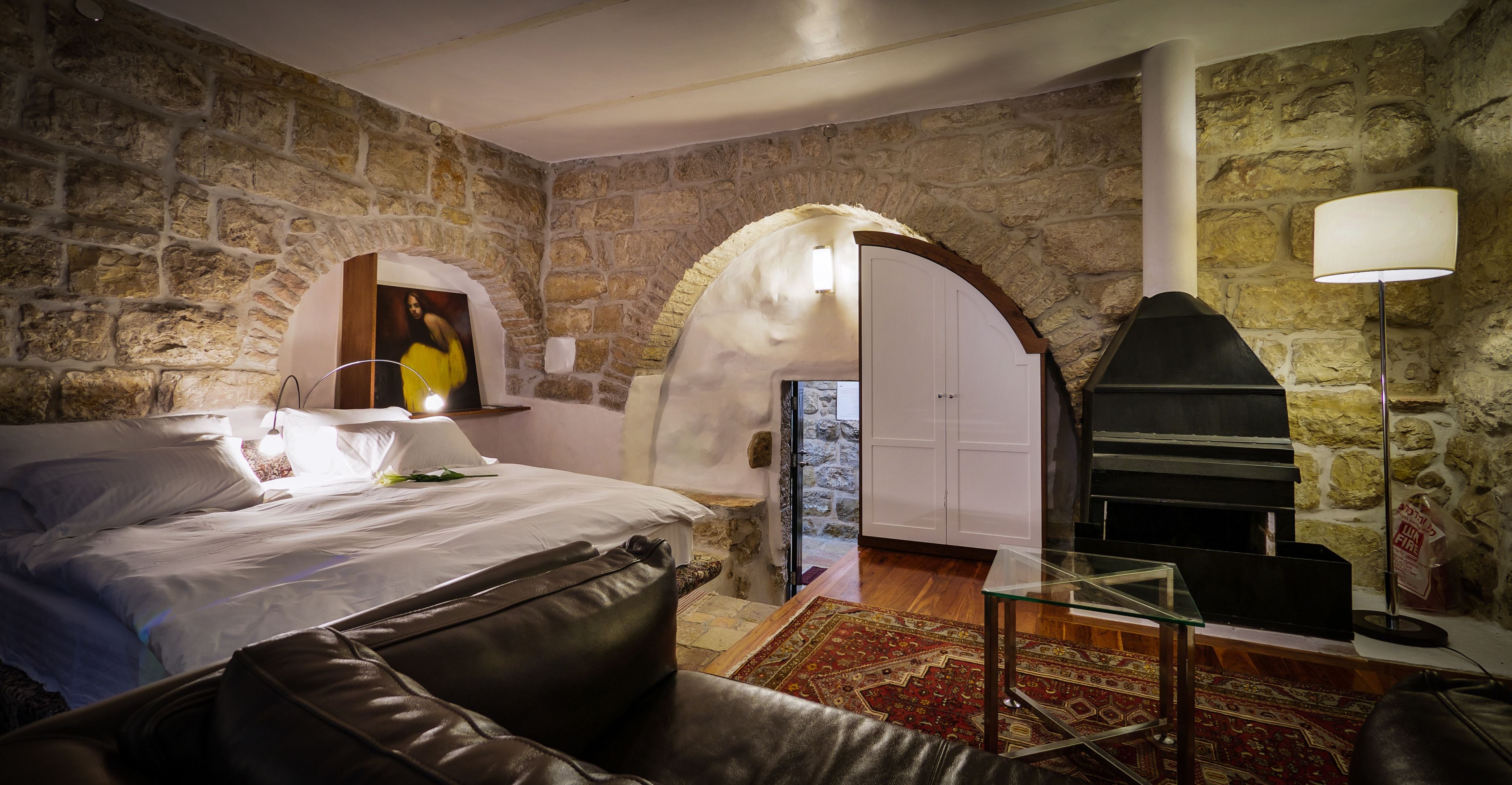 Ein Schlafzimmer mit Steinwänden, einem Bett, einem Glastisch und einem Kamin.