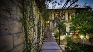Una escalera de piedra que conduce a un edificio con barandilla de hierro forjado y un jardín con macetas de plantas y flores.