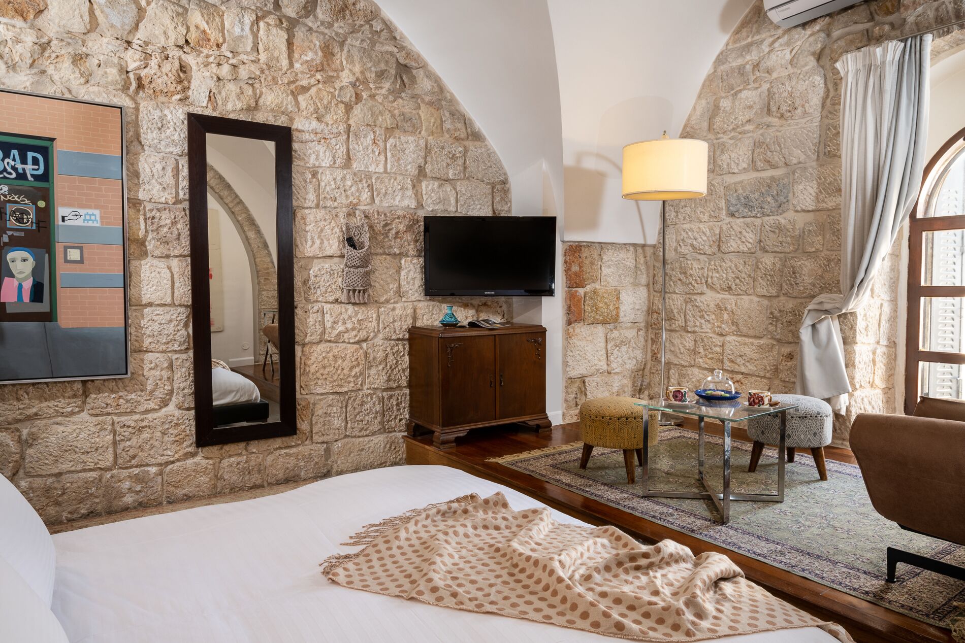 A cozy room with a stone wall, a bed, a TV, a wooden cabinet, and a small table with a lamp.