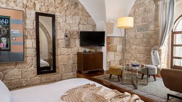 A cozy room with a stone wall, a bed, a TV, a wooden cabinet, and a small table with a lamp.