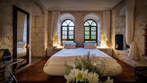 Un dormitorio con una cama grande, dos ventanas con cortinas, un espejo, una mesita de noche y un televisor.