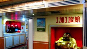 A hotel lobby with a reception desk, a statue of a golden figure, and a sign reading "1加1旅館". - One Plus One Hotel (Taipei)