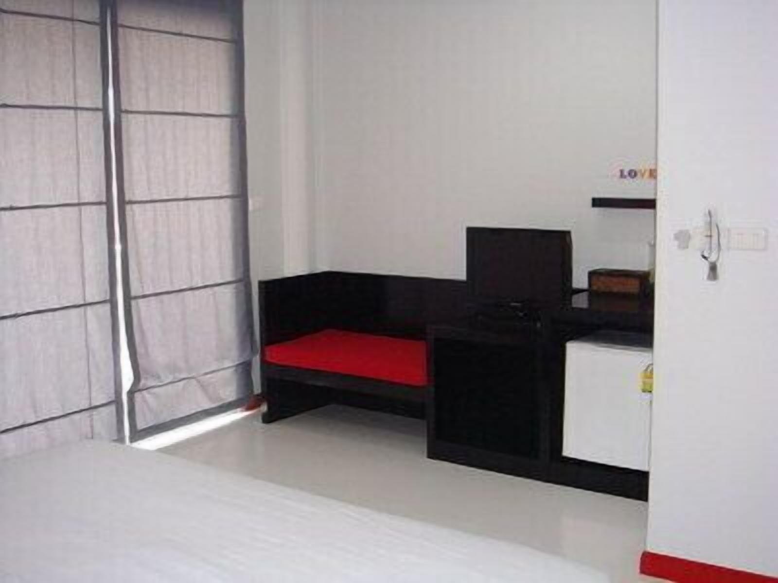 A room with a bed, a black and red sofa, a desk, and a wardrobe.