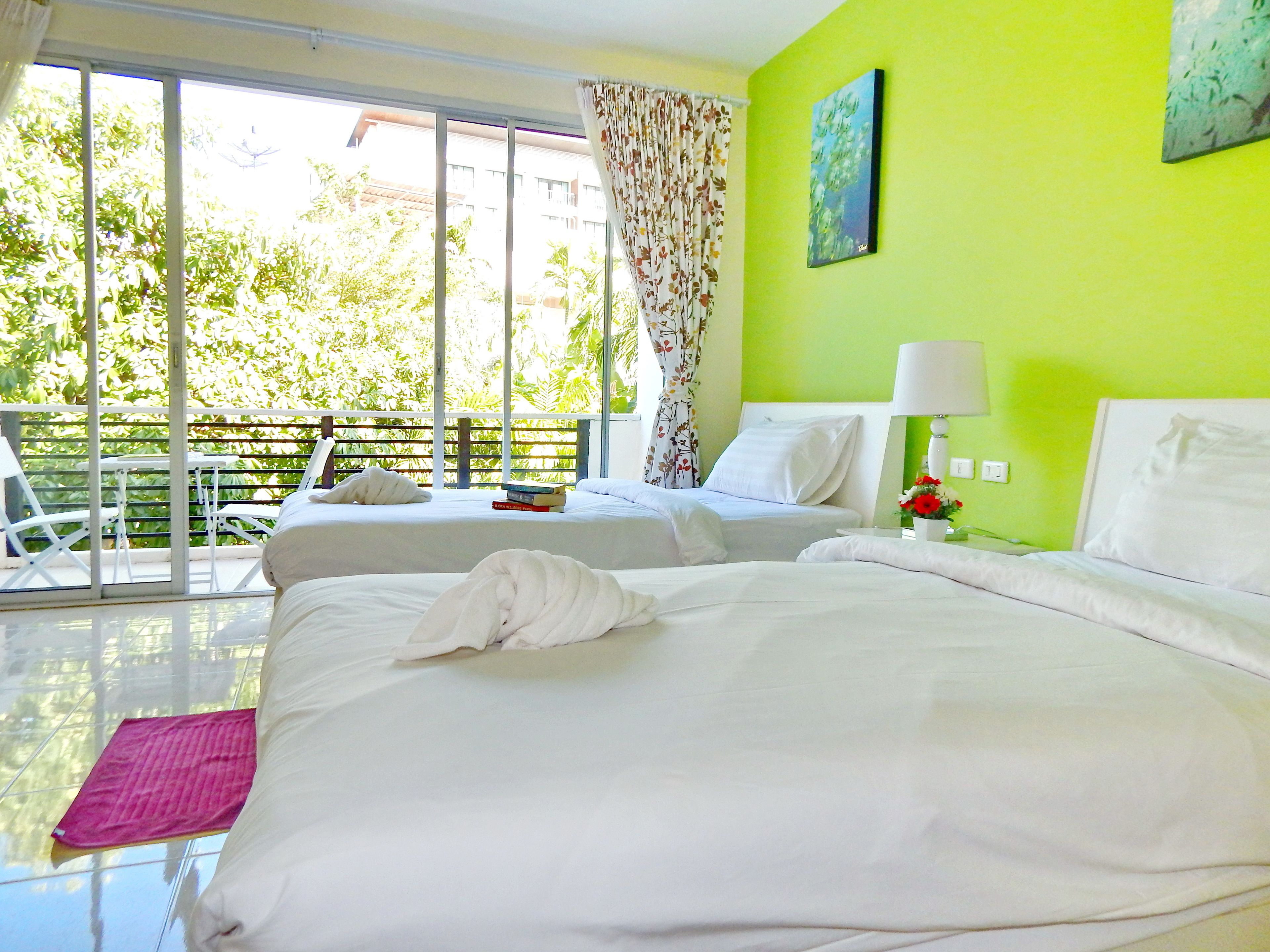 Een hotelkamer met twee bedden, een balkon en uitzicht op groen.