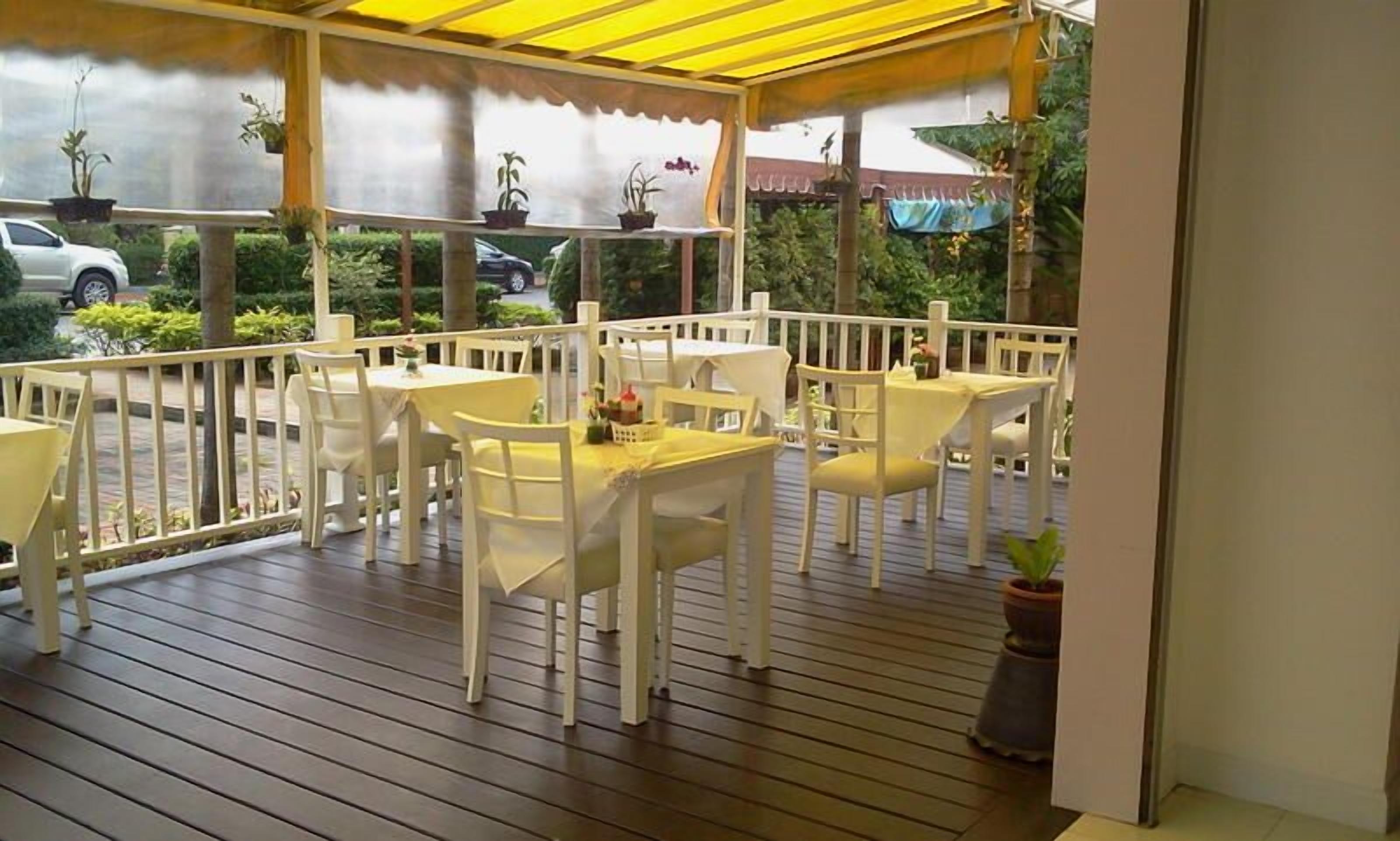 An outdoor patio with white tables and chairs, covered by a yellow canopy.
