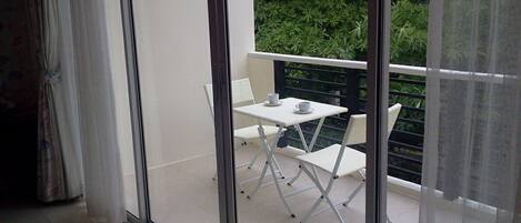 A balcony with a white table and chairs, a white cup, and a white saucer.