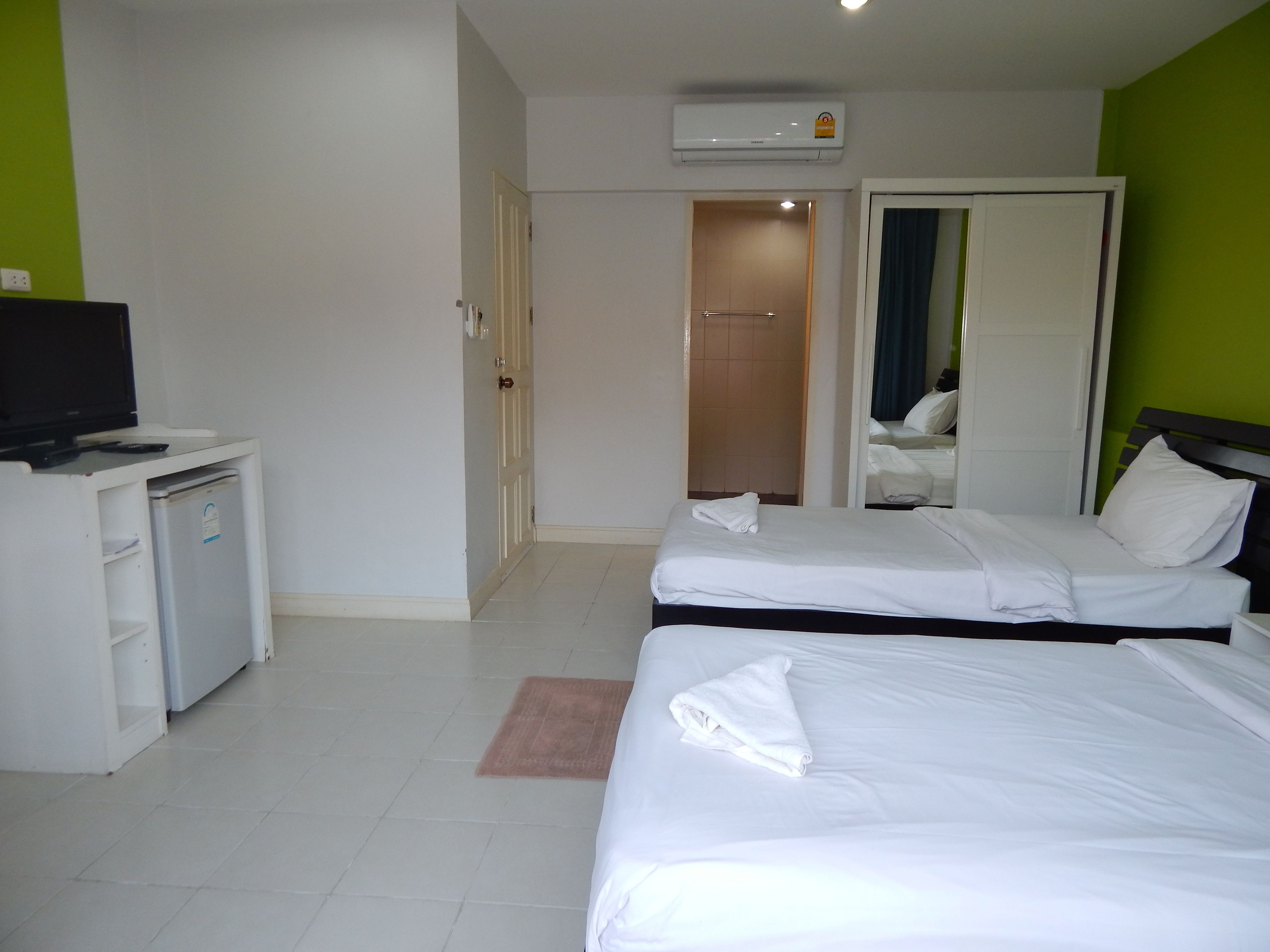 Una habitación de hotel con dos camas, un escritorio con televisor y un espejo.