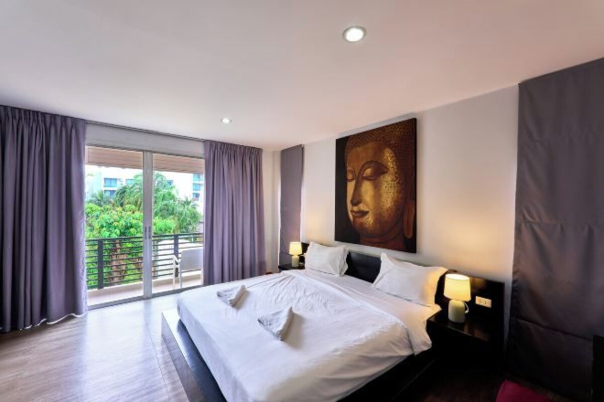 Habitación de hotel con una cama grande, vistas a la vegetación desde el balcón y una estatua de Buda en la pared.