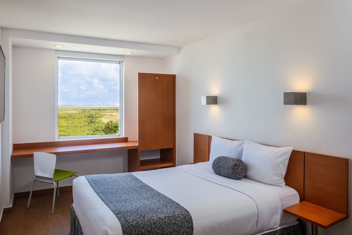 Habitación de hotel con cama, escritorio, silla, armario y una ventana grande con vistas.