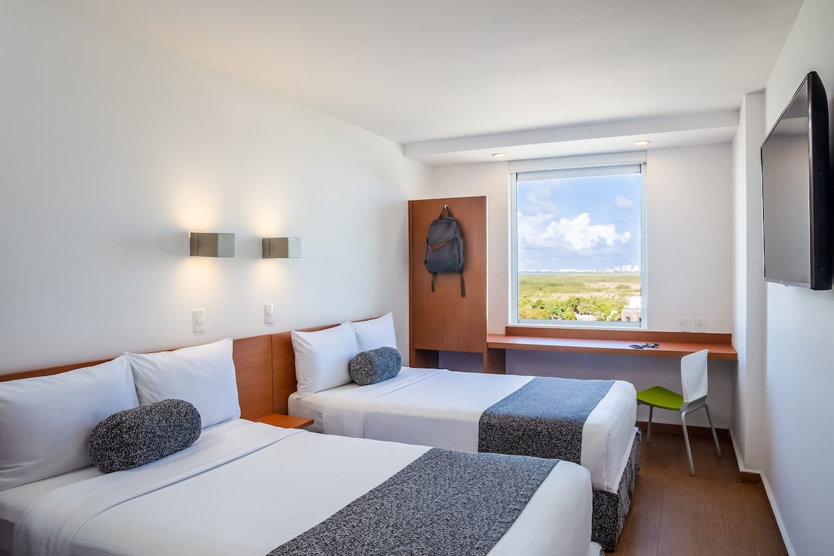 Habitación de hotel con dos camas, un escritorio, una silla, un televisor y ventana con vistas.