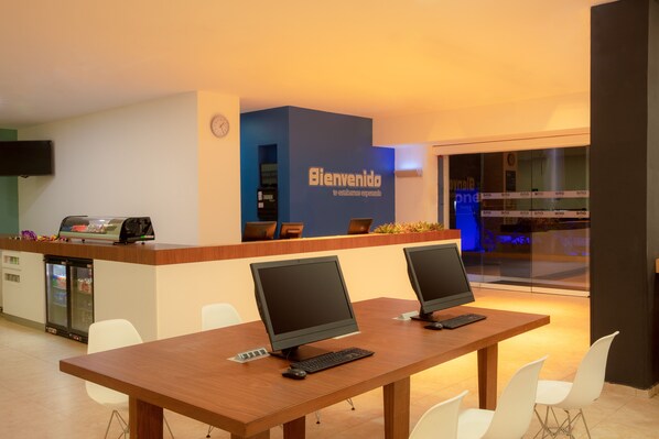 Un área de recepción con una pared azul, dos monitores de computadora, un mostrador y un reloj.