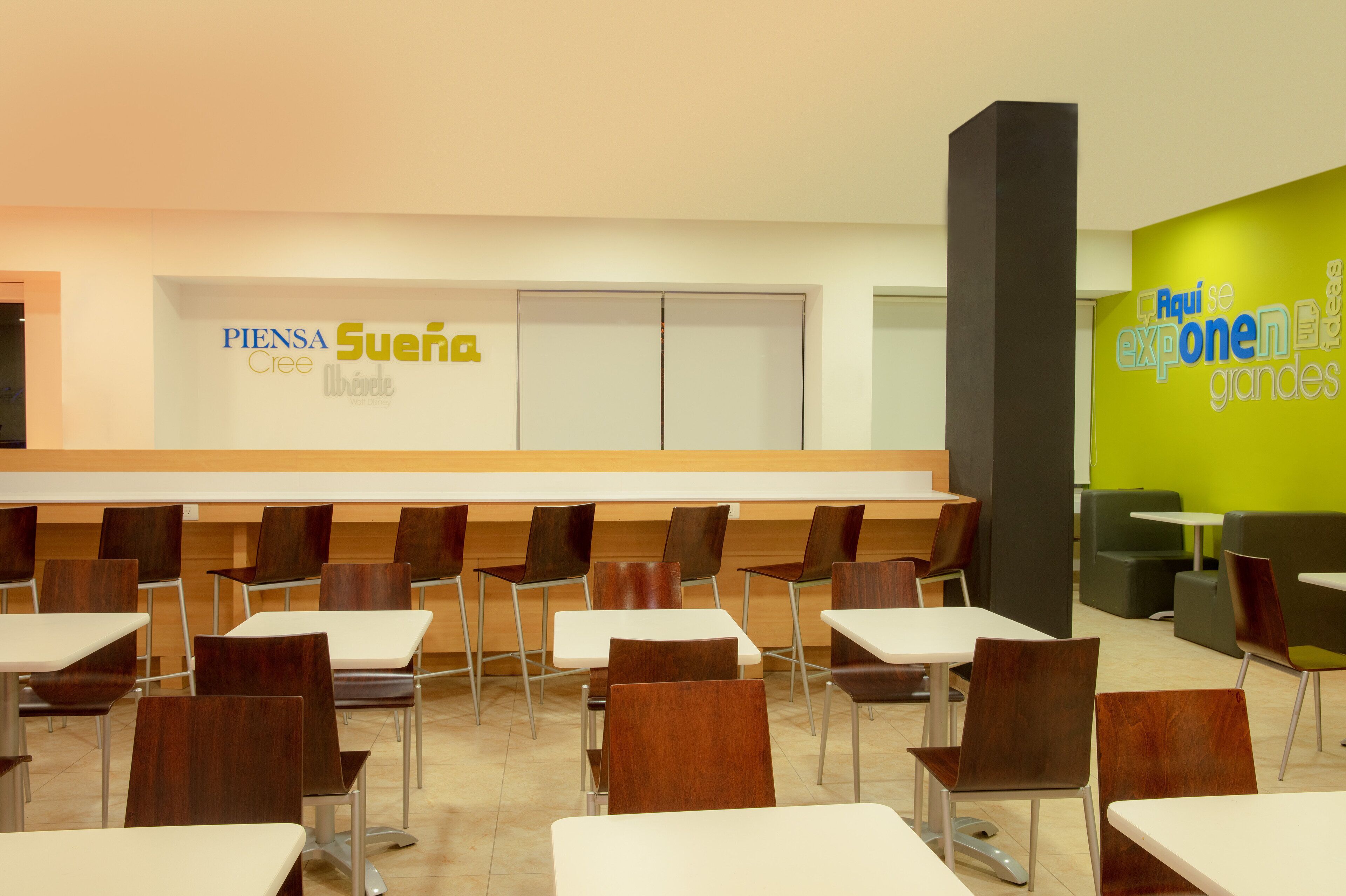 A modern dining area with tables and chairs, a counter with signage, and a bright green accent wall.