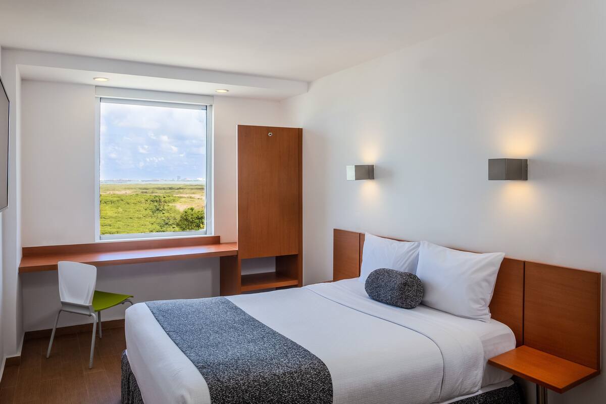 Habitación de hotel con una cama grande, un escritorio con una silla, un armario y vistas al exterior.