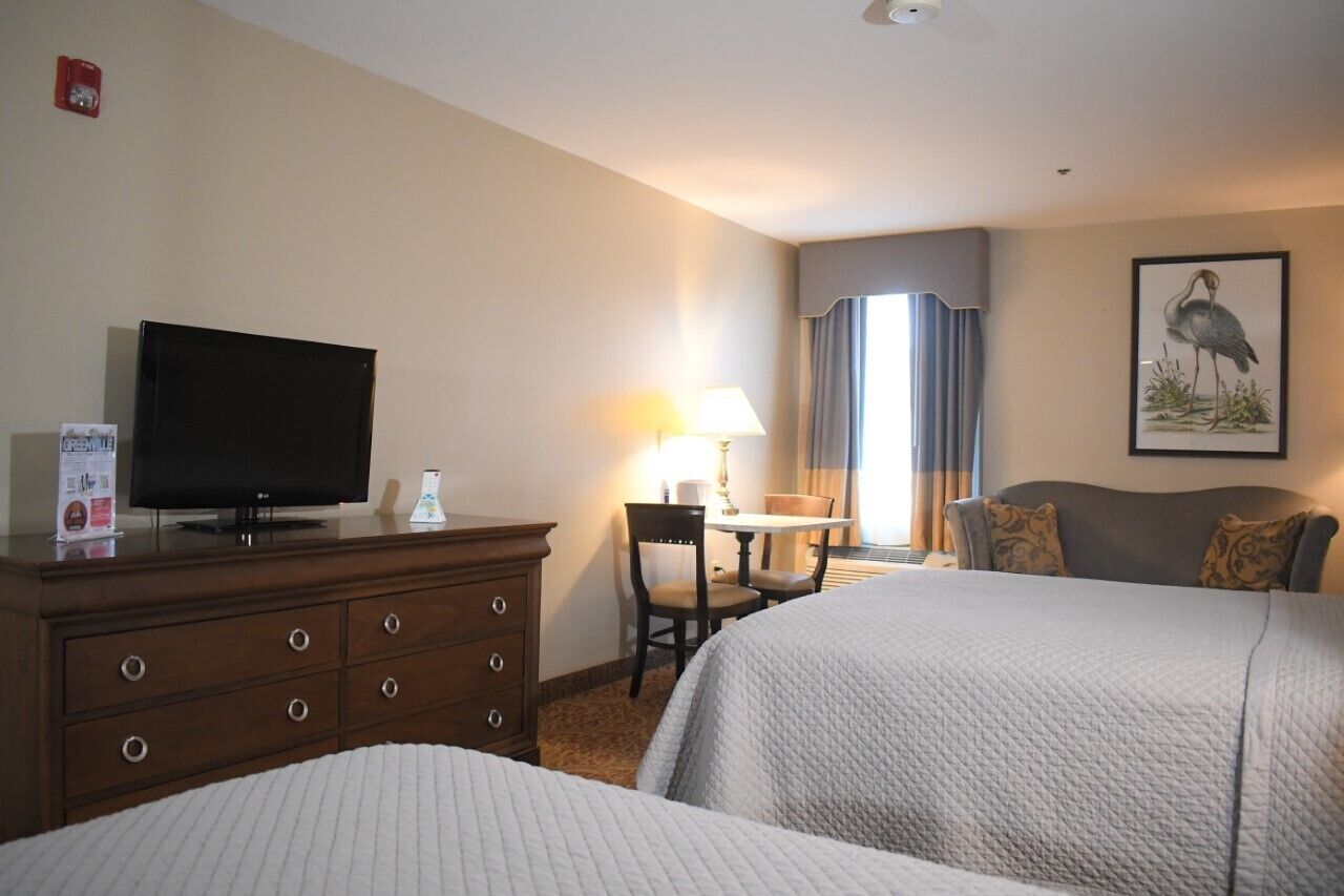 Een hotelkamer met twee bedden, een televisie op een dressoir, een bureau met een lamp en een raam met gordijnen.