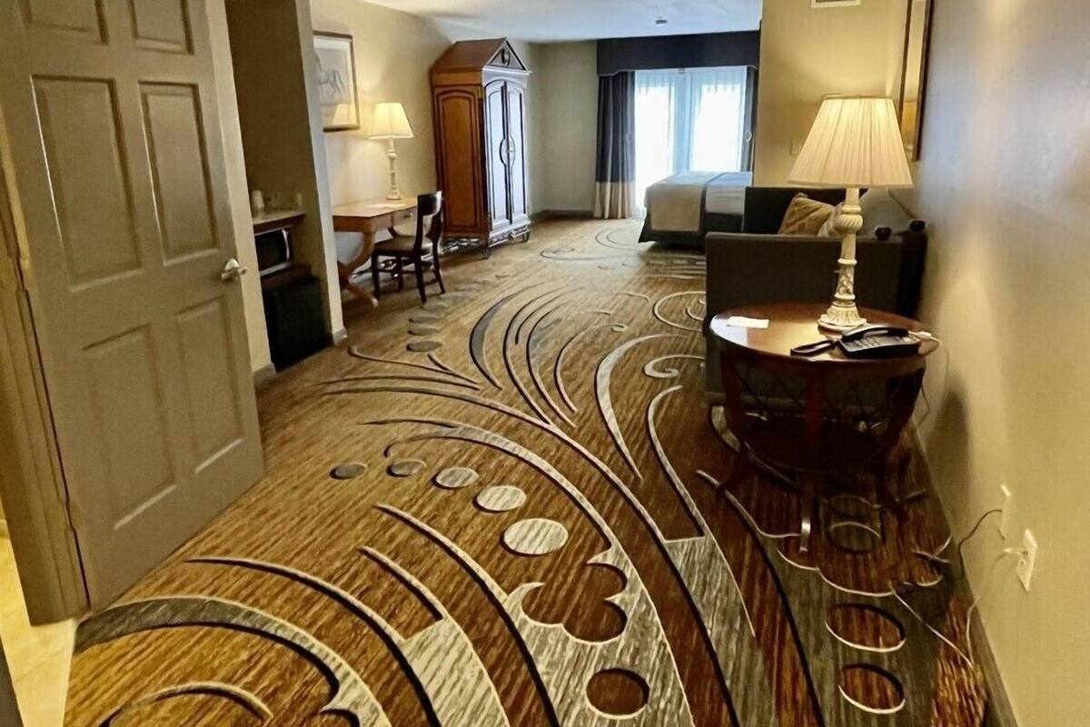 A hotel room with a carpeted hallway, a dining area with a table and chairs, and a bed with a headboard.