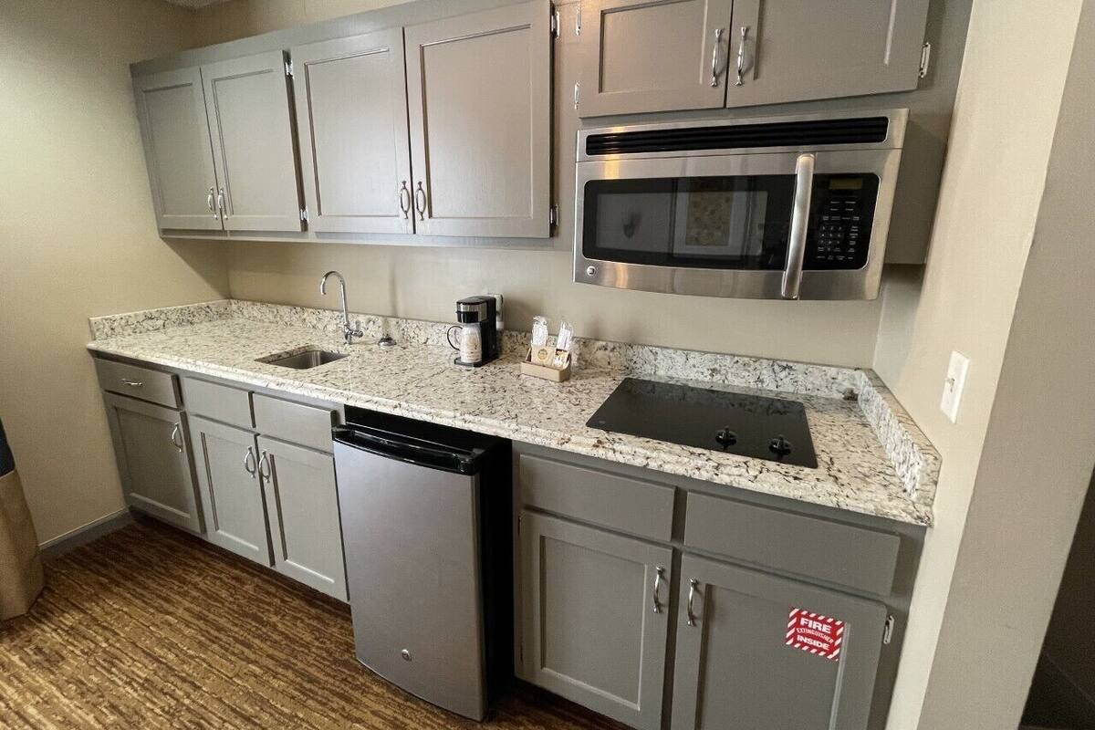 A compact kitchen with grey cabinets, a stainless steel microwave, a dishwasher, and a granite countertop.