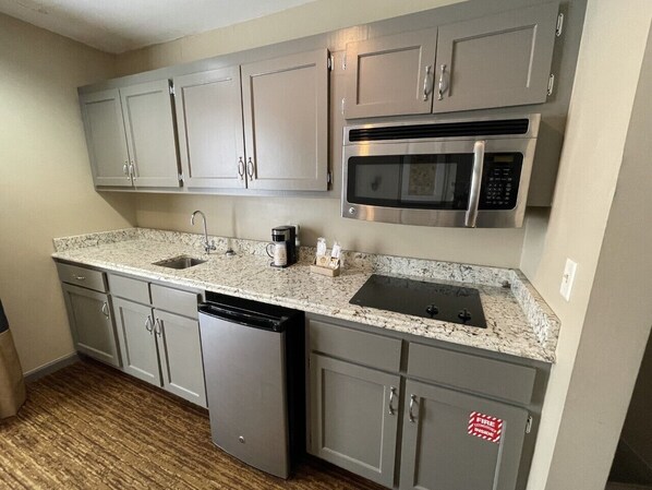 A compact kitchen with grey cabinets, a stainless steel microwave, a dishwasher, and a granite countertop.