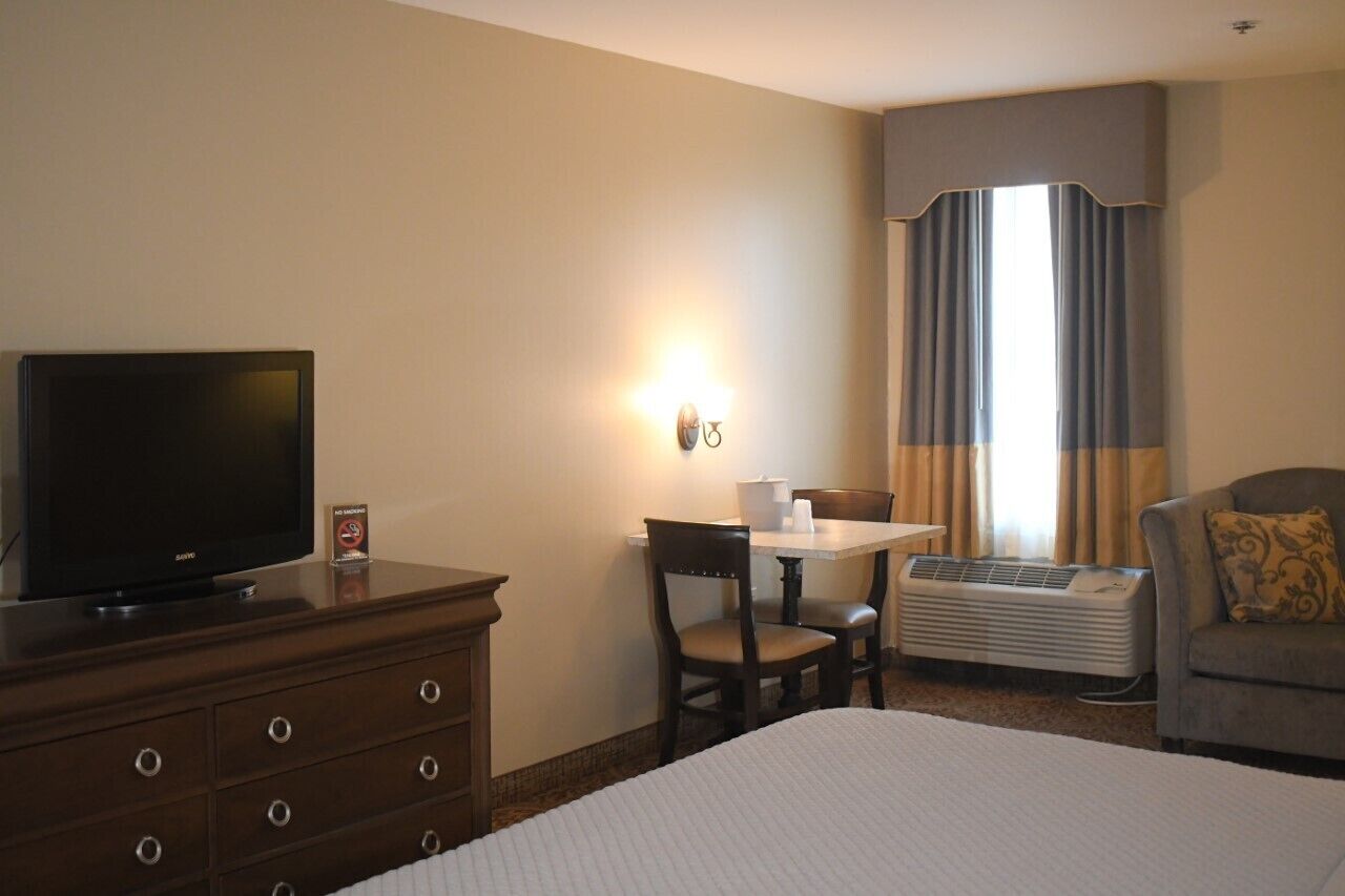 A hotel room with a bed, a TV on a dresser, a table with chairs, and an air conditioner.