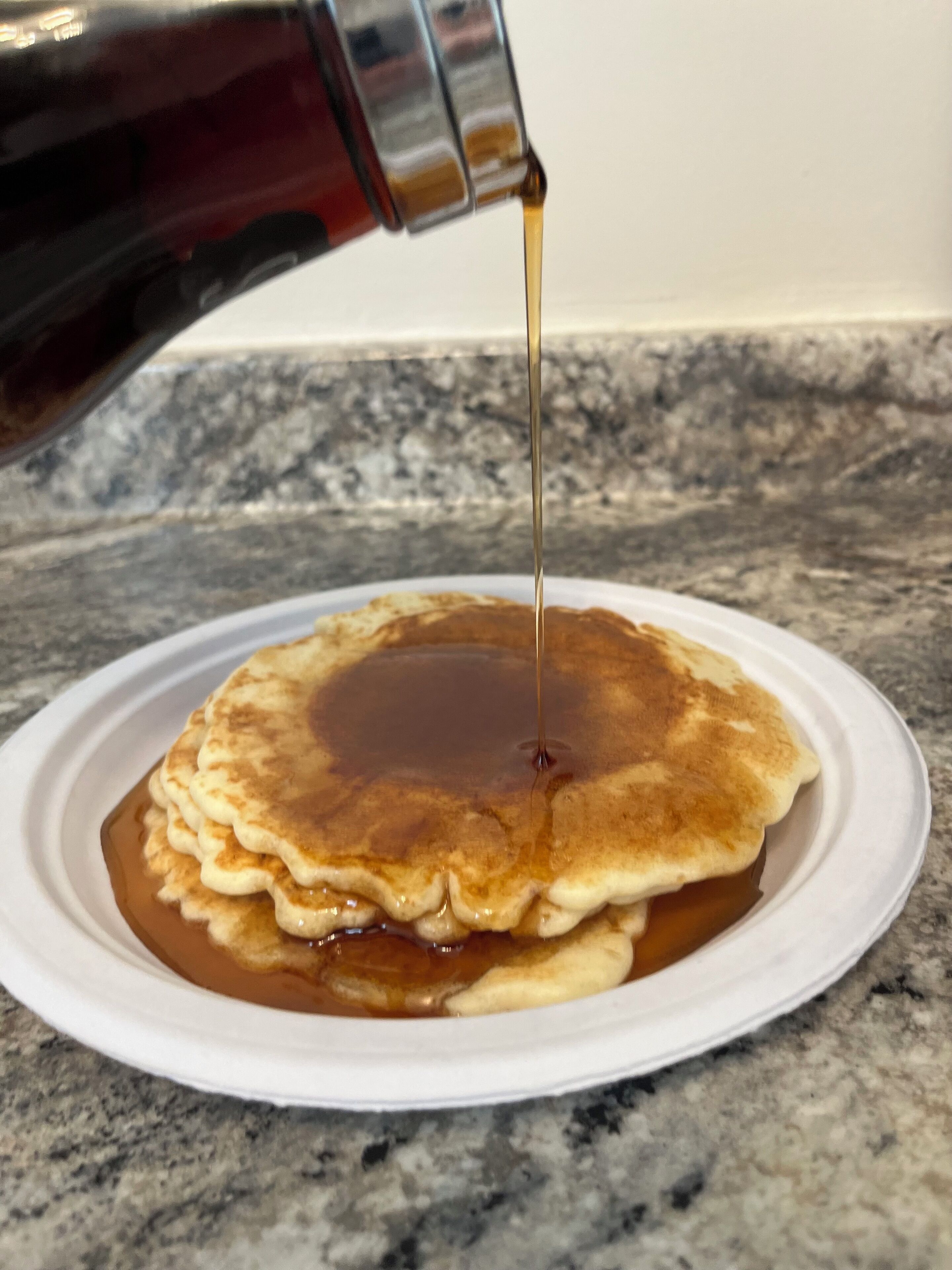 Pancakes stacked on a plate with syrup being poured over them.