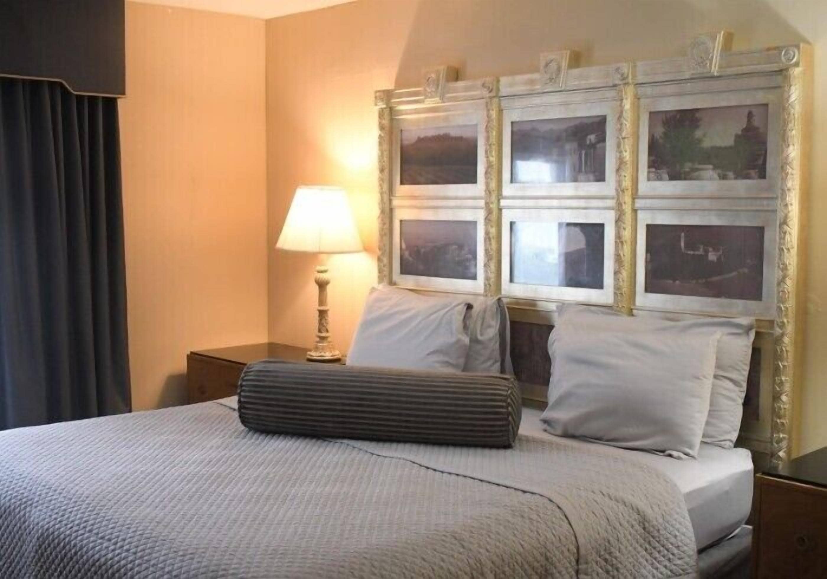 A neatly made bed with a grey quilt, a bedside lamp, and a headboard with framed pictures.