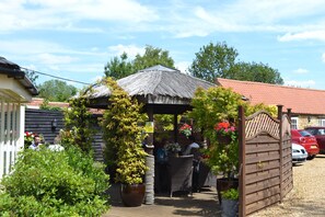 A covered outdoor seating area with wicker furniture, potted plants, and a wooden gate.