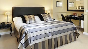 Una cama bien hecha con ropa de cama a rayas, una mesita de noche con lámpara, un escritorio con espejo y una silla.