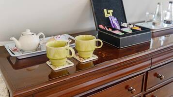 Un aparador de madera con un hervidor, dos tazas amarillas y una caja de cartas.