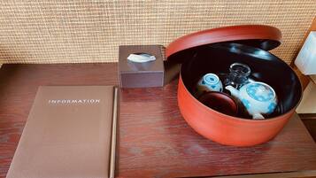 A wooden table with a brown folder labeled "INFORMATION" and a red container with a lid containing a teapot and cups.