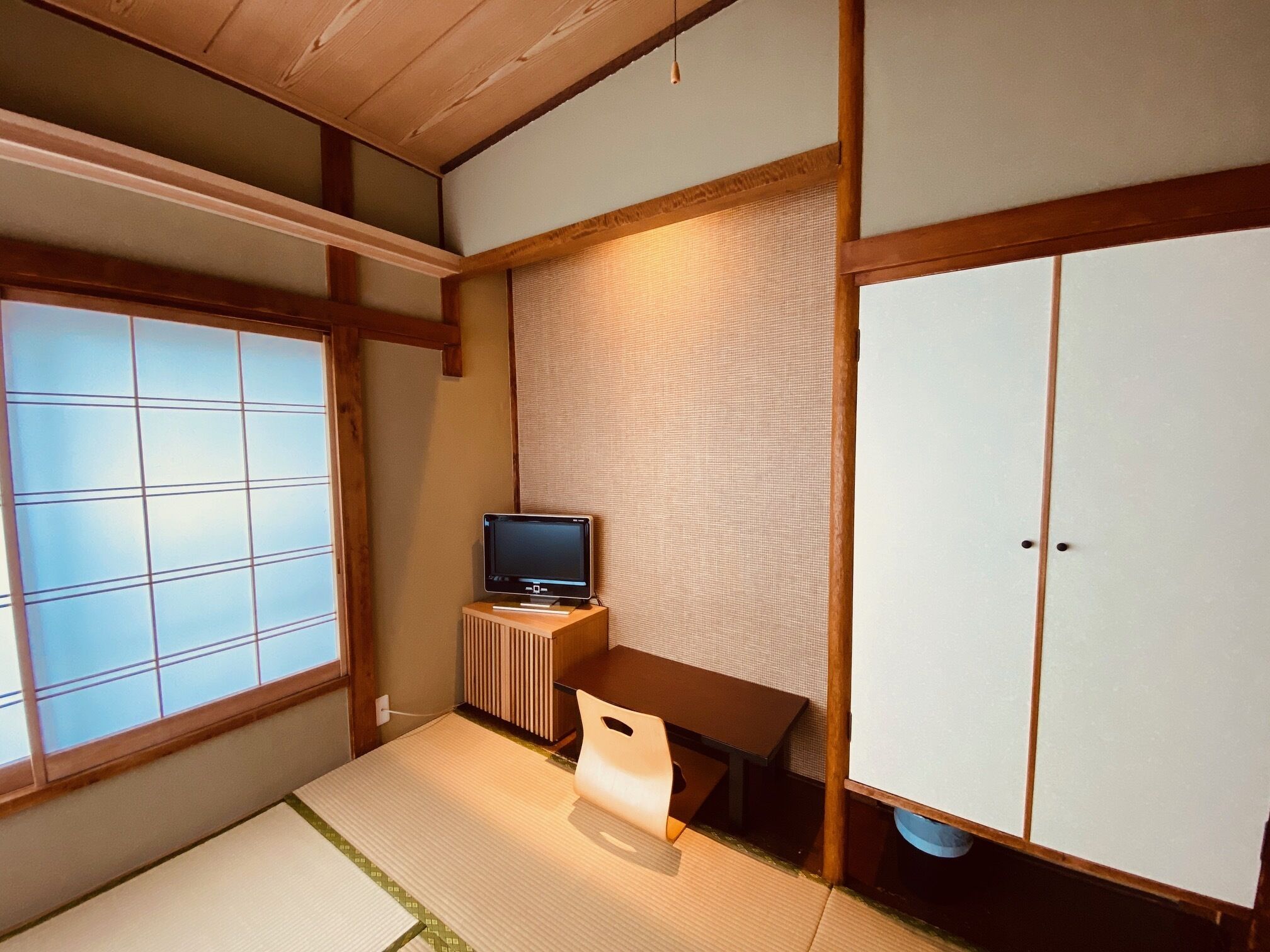 Una habitación japonesa tradicional con suelo de tatami, una mesa baja con televisor y puertas correderas.