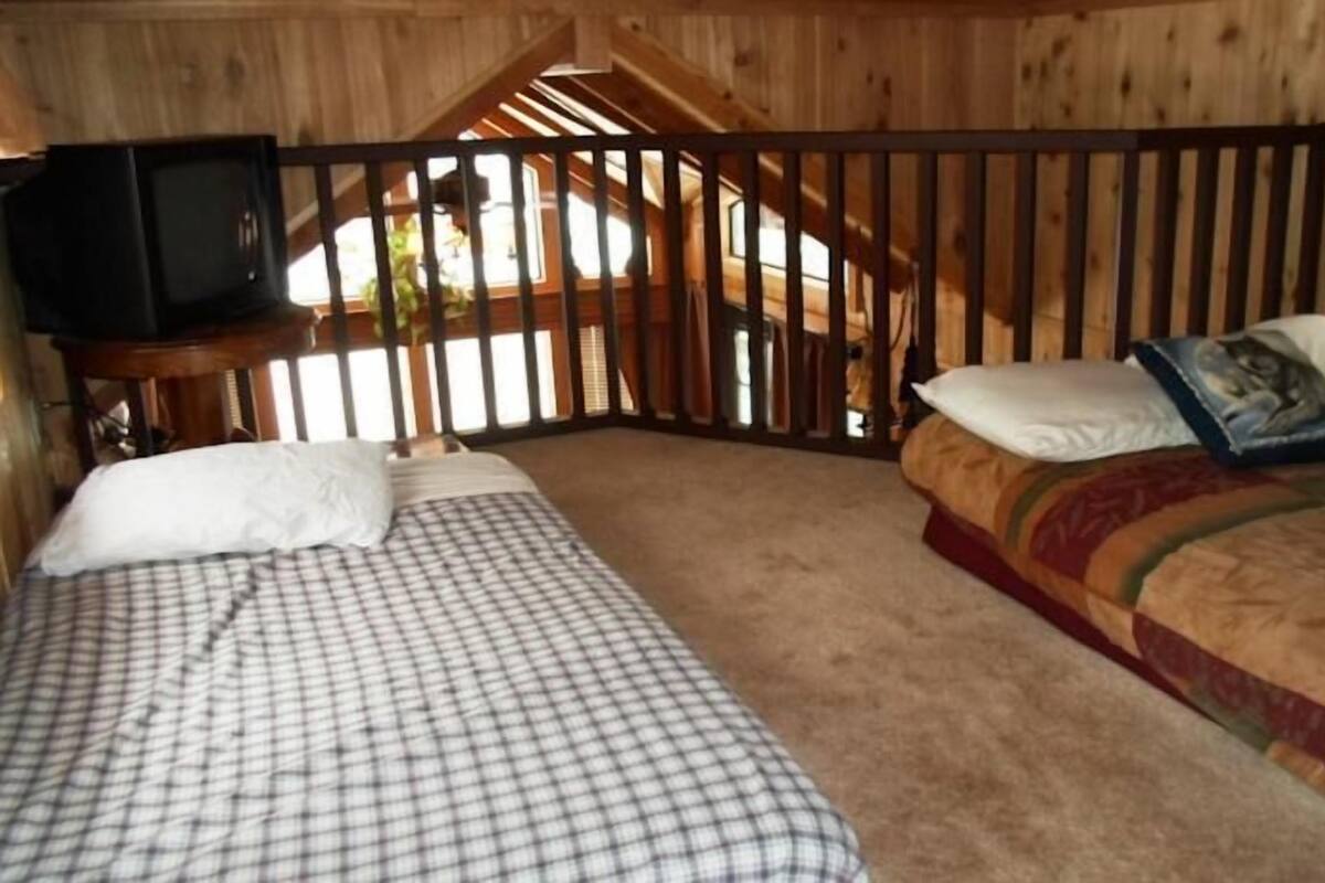 A bedroom with two beds, a television on a wooden table, and a window with blinds.