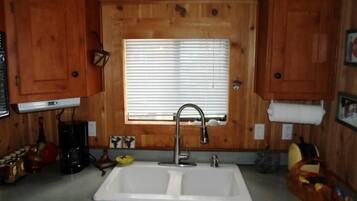 Una cocina con armarios de madera, un lavamanos doble, una ventana con persianas y una cafetera.