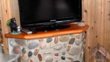 A television on a stone and wood entertainment unit with a bear figurine and remote controls.