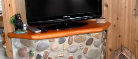 A television on a stone and wood entertainment unit with a bear figurine and remote controls.