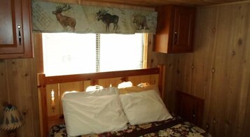 Una habitación de cabaña de madera con una cama, una ventana con cortina de estampado animal y un mueble auxiliar pequeño.