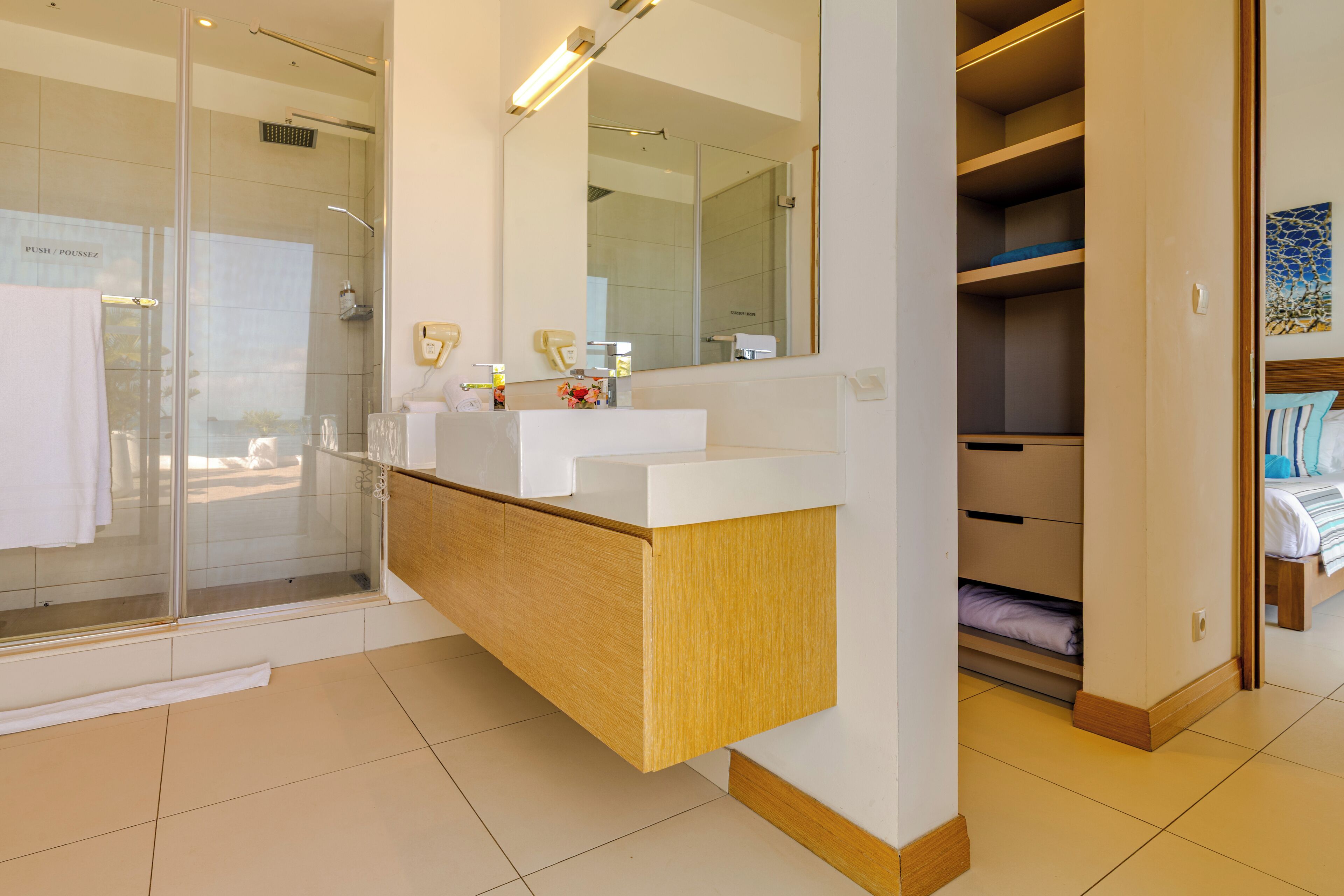 A modern bathroom with a glass shower enclosure, a wooden vanity, and a walk-in closet with built-in shelves.