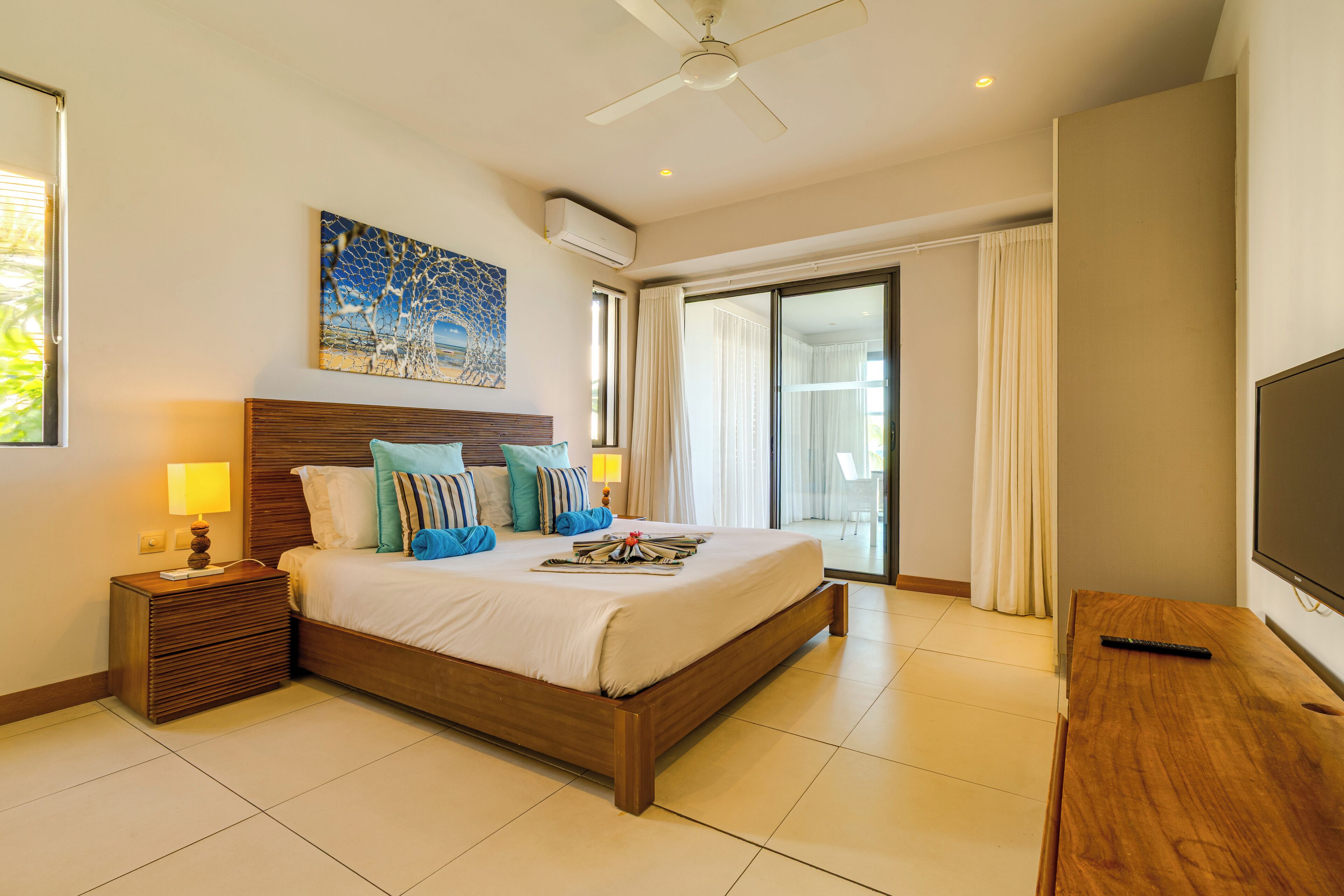 A modern hotel room with a large bed, a flat-screen TV, a ceiling fan, and a balcony with curtains.