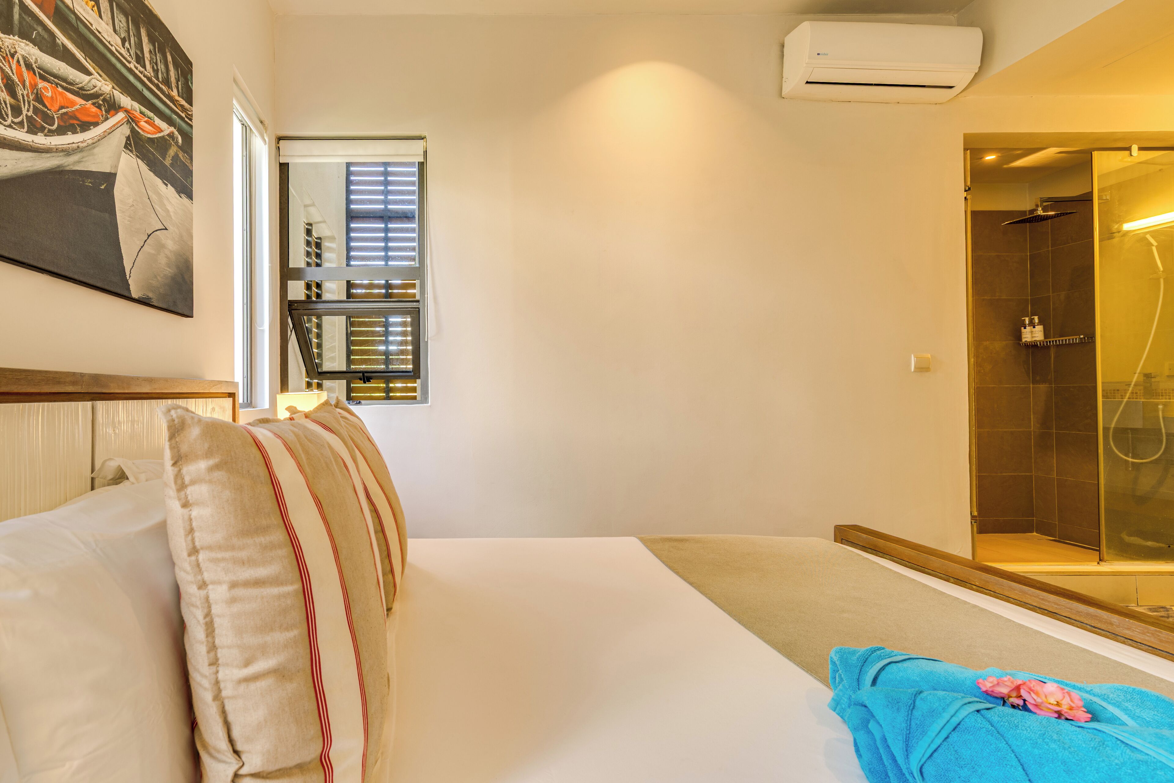 A hotel room with a bed, a bathroom with a glass-enclosed shower, and a painting on the wall.