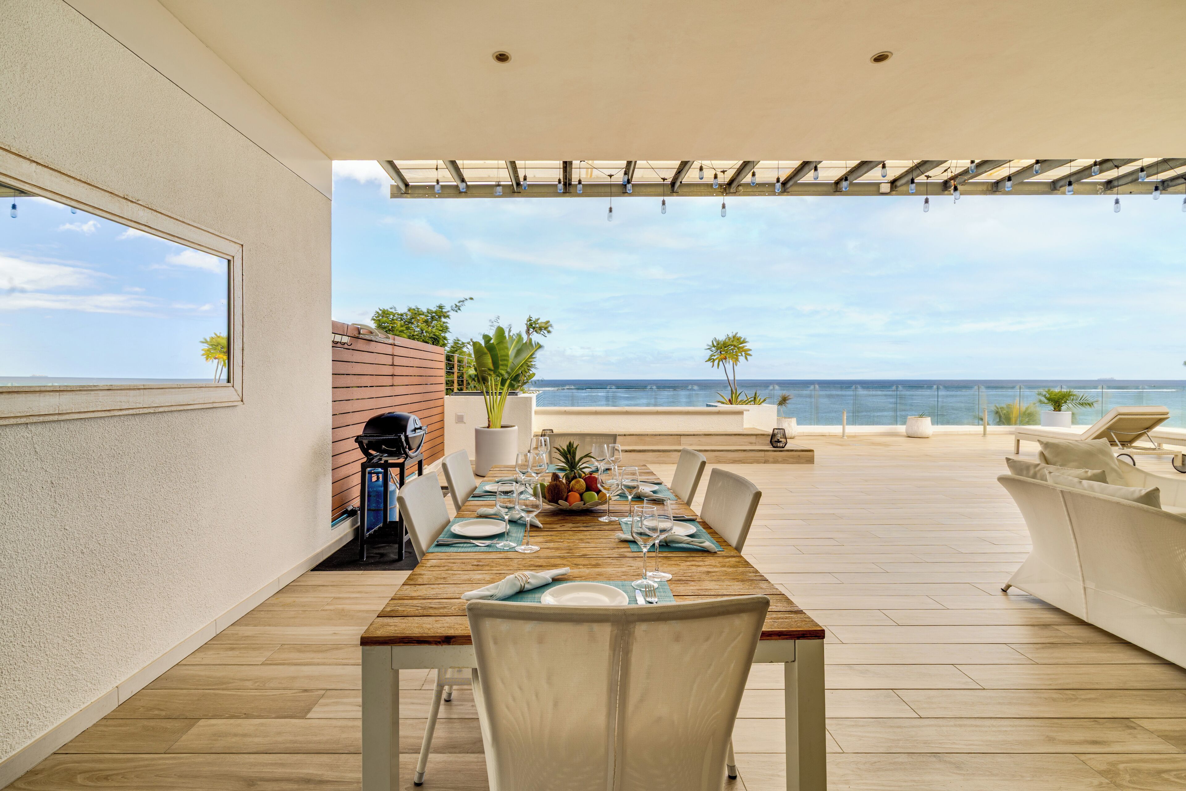 Comedor con mesa de madera dispuesta para seis personas, con vistas a una piscina y al mar.