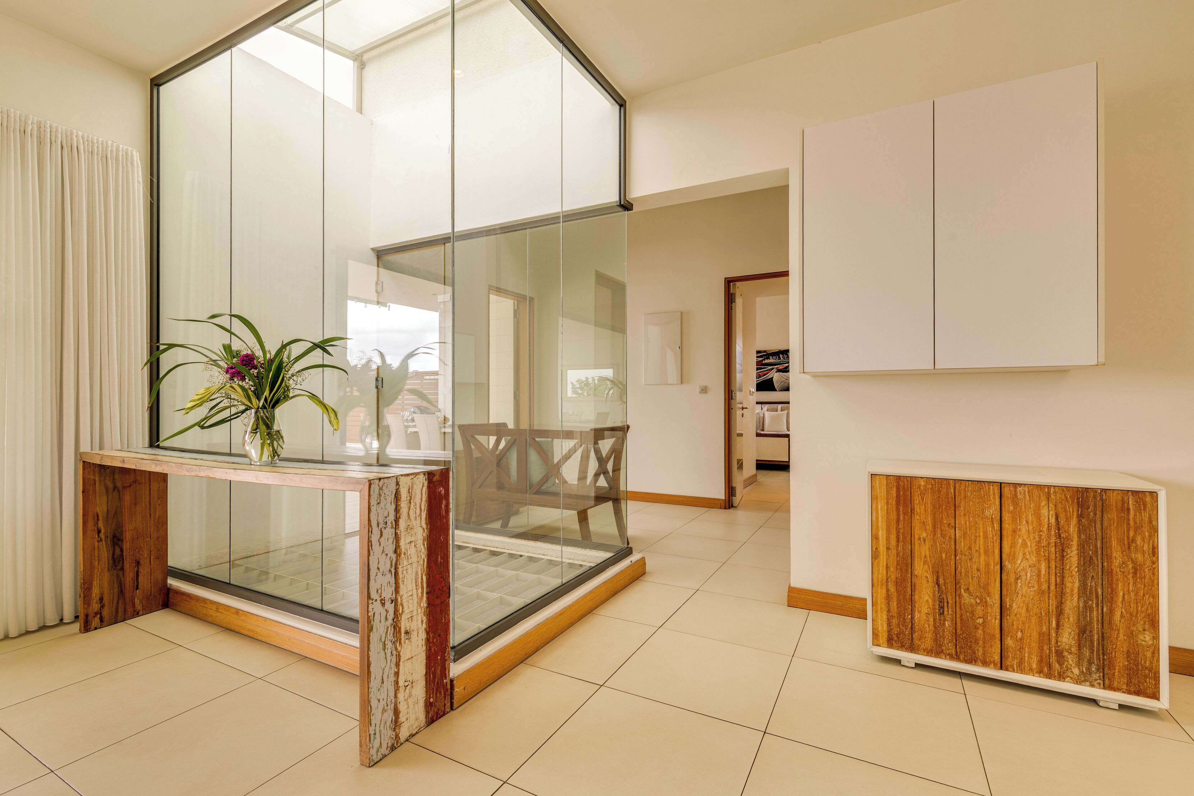 A modern living room with a glass partition, a wooden console table with a vase, and a wooden cabinet.